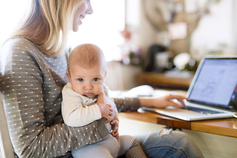 Mother with baby at home using laptop stock photo