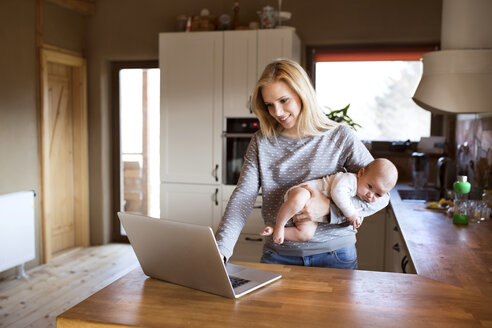 Lächelnde Mutter mit Baby in der Küche am Laptop - HAPF01396