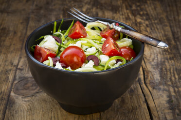 Bowl of zucchini spaghetti with feta, cherry tomatoes and black olives on wood - LVF05982