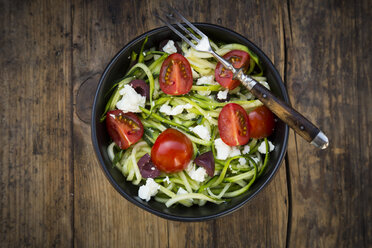 Schüssel mit Zucchini-Spaghetti mit Feta, Kirschtomaten und schwarzen Oliven auf Holz - LVF05983