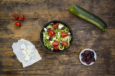 Schüssel mit Zucchini-Spaghetti mit Feta, Kirschtomaten und schwarzen Oliven auf Holz - LVF05984