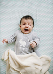 Portrait of crying baby girl lying on bed - GEMF01554