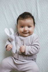 Porträt eines lächelnden kleinen Mädchens auf dem Bett liegend mit einem Spielzeughasen - GEMF01557
