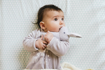 Baby girl lying on bed cuddling with toy bunny - GEMF01559