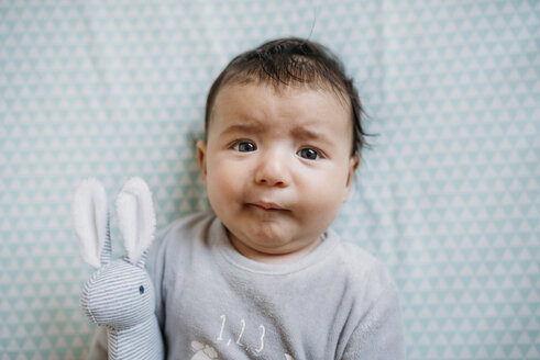 Porträt von Baby-Mädchen auf dem Bett liegend mit Spielzeug-Häschen ziehen lustiges Gesicht - GEMF01561