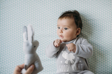 Baby-Mädchen liegt auf Krippe Blick auf Hand hält Spielzeug Hase - GEMF01564