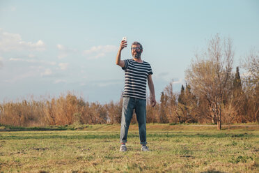 Man standing on a meadow taking photo with smartphone - RTBF00800