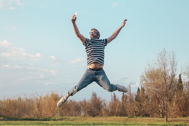 Man jumping in the air while taking photo with smartphone - RTBF00801