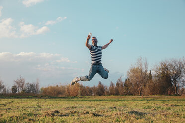 Smiling man jumping in the air while taking photo with vintage camera - RTBF00802