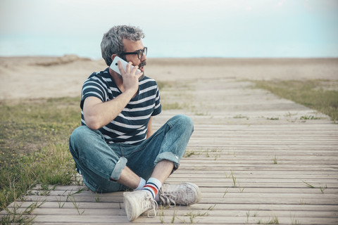 Mann am Telefon sitzt auf der Promenade und schaut in die Ferne, lizenzfreies Stockfoto