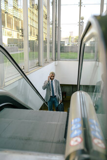 Geschäftsmann steht auf der Rolltreppe und telefoniert mit seinem Smartphone - DAPF00606