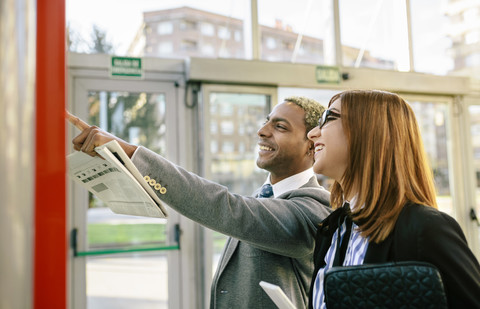 Junger Geschäftsmann und Frau schauen im Fahrplan der öffentlichen Verkehrsmittel nach, lizenzfreies Stockfoto