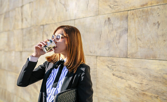 Geschäftsfrau mit Sonnenbrille, die einen Kaffee zum Mitnehmen trinkt - DAPF00620