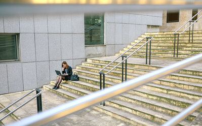 Geschäftsfrau sitzt auf einer Treppe und benutzt einen Laptop - DAPF00642