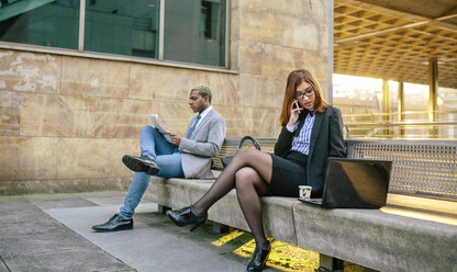 Young businessman and woman sitting on bench, woman talking on the phone - DAPF00645