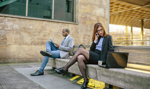 Junger Geschäftsmann und Frau sitzen auf einer Bank, Frau telefoniert - DAPF00645