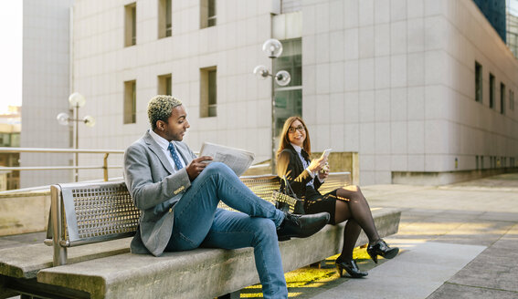 Junger Geschäftsmann und Frau sitzen auf einer Bank und unterhalten sich - DAPF00646