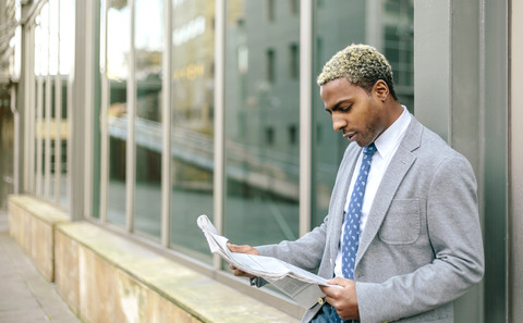 Businessman leaning against wall, reading newspaper stock photo