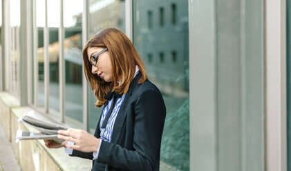 Businesswoman standing in front of wall, reading newspaper - DAPF00656