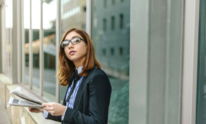 Businesswoman standing in front of wall, reading newspaper - DAPF00657