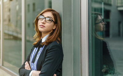 Businesswoman leaning against window with arms crossed - DAPF00658