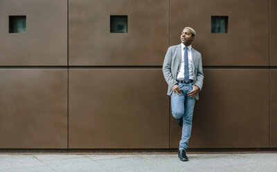 Businessman standing in front of wall with hands in pockets - DAPF00660