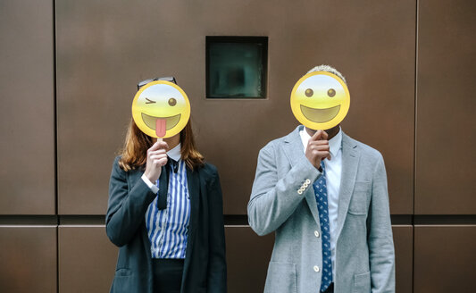 Junger Geschäftsmann und Frau bedecken Gesichter mit Emoji-Masken - DAPF00669