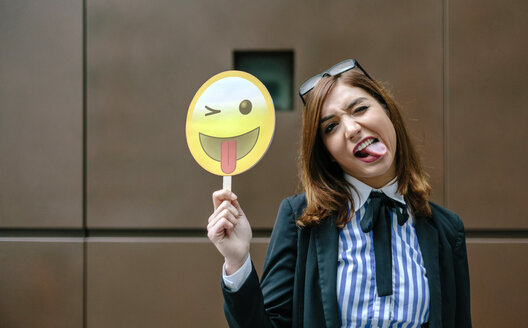Geschäftsfrau hält Emoji lächelnd mit heraushängender Zunge - DAPF00670
