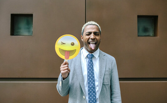 Geschäftsmann hält Emoji lächelnd mit herausgestreckter Zunge - DAPF00672