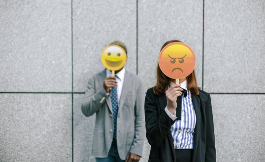 Young businessman and woman covering faces with emoji masks - DAPF00673