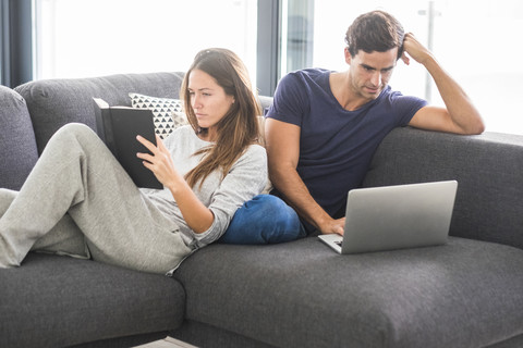 Junges Paar auf Couch mit Buch und Laptop, lizenzfreies Stockfoto