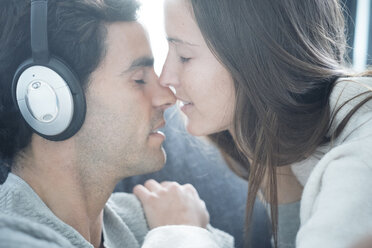 Junge Frau küsst Mann mit Kopfhörern zu Hause - SIPF01560