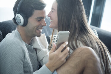 Happy young couple with headphones and smartphone at home - SIPF01561