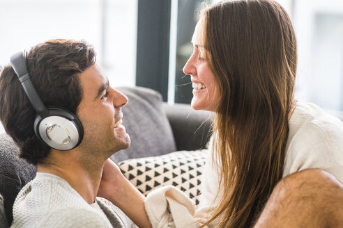 Lächelnde junge Frau betrachtet einen Mann, der zu Hause Kopfhörer trägt - SIPF01562