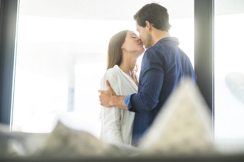 Junges verliebtes Paar, das sich am Fenster küsst, lizenzfreies Stockfoto