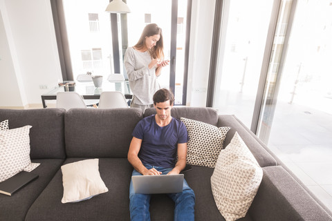 Junges Paar zu Hause mit Handy und Laptop, lizenzfreies Stockfoto