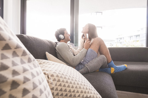 Glückliches junges Paar mit Kopfhörern und Smartphone auf der Couch, lizenzfreies Stockfoto