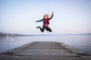 Blond woman jumping in the air on a jetty - SIPF01606