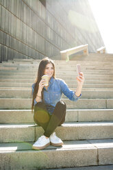 Junge Frau mit Kaffee zum Mitnehmen sitzt auf der Treppe und macht ein Selfie mit ihrem Smartphone - VABF01298