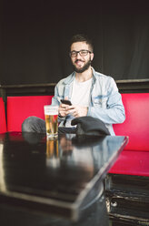 Portrait of smiling young man sitting in a pub - RAEF01809