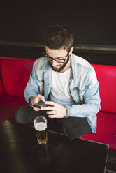 Young man sitting in a pub text messaging - RAEF01811