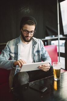 Junger Mann sitzt in einer Kneipe und benutzt ein Tablet - RAEF01813