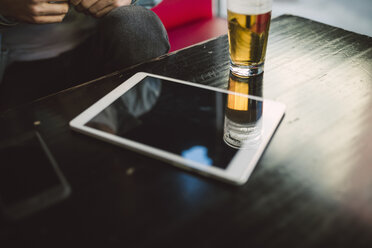 Tablet und Glas Bier auf dem Tisch - RAEF01815