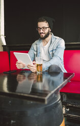 Smiling young man sitting in a pub using tablet - RAEF01816