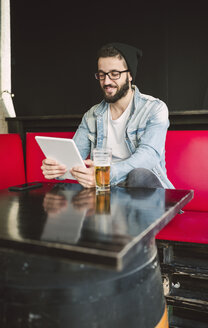 Lächelnder junger Mann, der in einer Kneipe sitzt und ein Tablet benutzt - RAEF01816