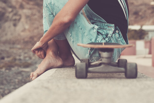 Frau mit Skateboard auf einer Mauer sitzend, Teilansicht - SIPF01611