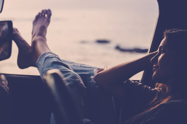 Dreaming woman sitting in car at sunset - SIPF01615