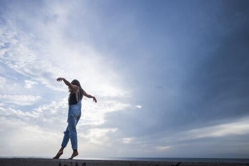 Woman with arms outstretched balancing on wall in front of sky - SIPF01616