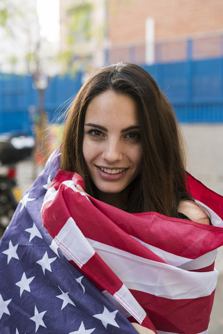 Porträt einer lächelnden jungen Frau, eingewickelt in die US-amerikanische Flagge, lizenzfreies Stockfoto