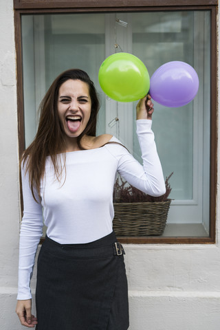 Porträt einer jungen Frau mit Luftballons, die die Zunge herausstrecken, lizenzfreies Stockfoto